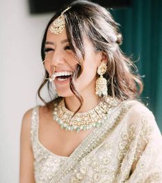 a woman in a white sari smiling and wearing gold jewelry