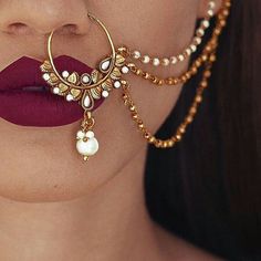 a close up of a person with red lipstick and gold jewelry on her face,