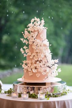 a pink wedding cake with white flowers on top and candles in the middle, sitting on a round table