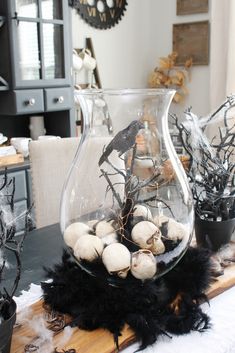 a glass vase filled with lots of white balls on top of a wooden table covered in black feathers