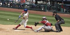 a baseball player swinging at a ball with the catcher and umpire behind him, during a game