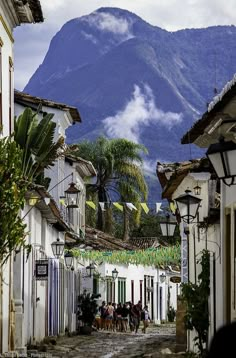 people are walking down an old cobblestone street with mountains in the back ground