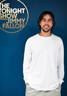 a man standing in front of a blue wall with the tonight show logo on it