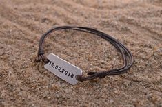 a close up of a bracelet on sand with a name tag hanging from it's end