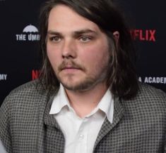 a man with long hair wearing a suit and white shirt is looking at the camera