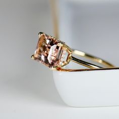 Beautiful emerald cut peachy pink color morganite ring, diamond hidden halo ring. DETAILS ABOUT THE RING!* 9x7mm emerald cut morganite is peach pink color.* Ring band is 1.3mm 14k solid yellow gold* Emerald cut 4 prong setting is 14k solid yellow gold* Set 20 white diamonds in the hidden halo, total 0.05 ct. weight. Rectangle Morganite Engagement Ring, Rose Gold Emerald Cut Topaz Ring, Emerald Cut Topaz Ring In Rose Gold, Radiant Cut Morganite Rings For Anniversary, Elegant Morganite Radiant Cut Rings, Emerald-cut Topaz Ring In Rose Gold, Formal Emerald Cut Morganite Jewelry, Elegant Radiant Cut Morganite Rings, Morganite Ring Emerald Cut