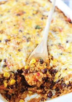 a casserole dish with beans, corn and cheese on the top has a wooden spoon in it