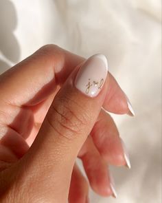 a woman's hand holding a white manicure with gold letters on it and the tip of her finger