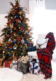 a christmas tree with presents under it in a living room next to a plaid blanket