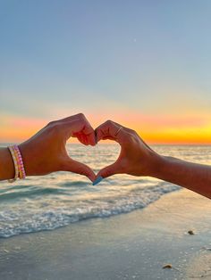 two people making a heart shape with their hands on the beach at sunset or sunrise