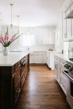 a large kitchen with white cabinets and wood flooring is pictured in this image, there are flowers on the counter