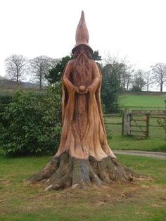 a statue of a woman standing on top of a tree stump in a park area