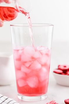 someone pouring water into a glass filled with ice and raspberries