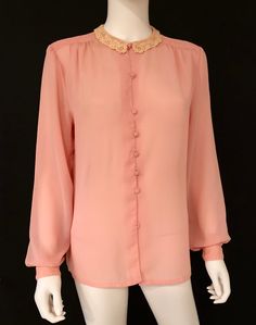 Vintage 1980s feminine long sleeve blouse in peach, featuring a delicate crocheted lace collar, pleating at shoulder tops, and a seven self covered button closure. Soft and with wonderful drape. Designer label removed; fabric label removed - feels like polyester. Retro feminine top, circa 1980s, is in excellent vintage condition. Bottom button missing; not visible when tucked in. Enjoy! *(International Buyers are welcome - however, please email me so I can check the shipping rate for you before Vintage Blouse With Lace Cuffs For Fall, Vintage Peach Tops For Spring, Peach Long Sleeve Blouse For Fall, Long Sleeve Peach Blouse For Fall, Pink Blouse With Lace Collar For Daywear, Retro Long Sleeve Tops With Lace Collar, Pink Long Sleeve Lace Top Blouse, Retro Long Sleeve Blouse With Lace Collar, Feminine Long Sleeve Peach Blouse