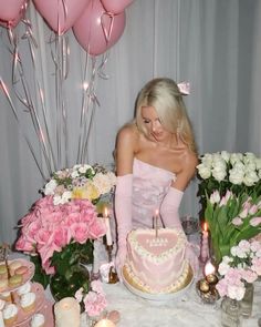 a woman sitting in front of a cake with candles on top of it, surrounded by flowers and balloons