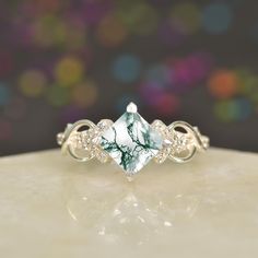 a ring with a green and white stone surrounded by diamonds on a table top in front of a blurry background