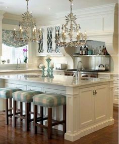 a kitchen island with stools and chandelier hanging from it's ceiling