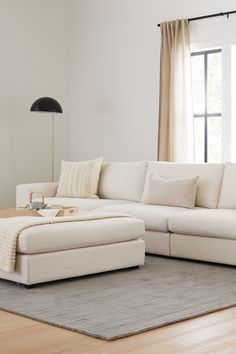 a living room with a large white sectional couch and ottoman in front of a window