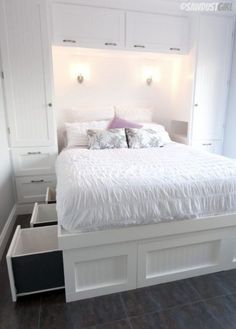 a white bed with drawers underneath it in the middle of a floored room,