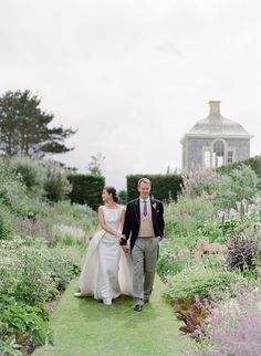 a bride and groom walking through the garden