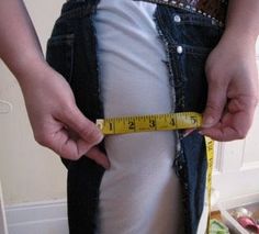 a person is measuring their waist with a tape around his waist and there are vegetables in the background