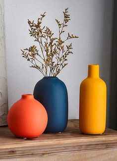 three different colored vases sitting on a shelf