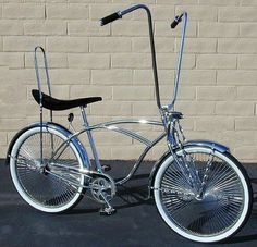 a silver bicycle parked in front of a brick wall with a black seat and handlebars