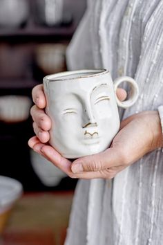 a woman holding a white ceramic cup with a face drawn on it's side