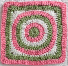 a crocheted square with a green and pink design on the center, sitting on a white surface