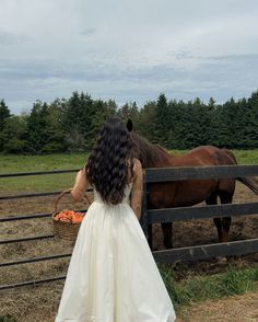 a woman in a white dress standing next to a horse near a fence with carrots