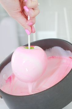 a person is dipping an apple into pink liquid in a black bowl with a toothpick