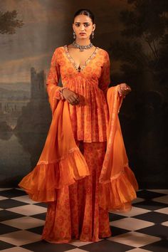 Tangerine peplum kurta with floral print and mirror, thread, pearl, bead, gota embroidered neckline. Paired with gharara and dupatta.
Components: 3
Pattern: Printed, Embroidery
Type Of Work: Floral, mirror, thread, pearl, bead, gota
Neckline: Plunge V neck
Sleeve Type: Full sleeves
Fabric: Georgette, Organza, Lining: Crepe
Color: Orange
Other Details: 
Length:
Kurta: 34 inches
Gharara: 42 inches
Sheer dupatta
Pleated frill hem
Occasion: Sangeet - Aza Fashions Designer Peplum Set In Georgette, Festive Mirror Work Peplum Anarkali Set, Anarkali Dress With Sheer Dupatta And Peplum Shape, Designer Georgette Sharara With Peplum, Georgette Peplum Sharara For Designer Events, Georgette Sharara With Peplum For Designer Wear, Designer Peplum Anarkali Set For Navratri, Navratri Designer Anarkali Set With Peplum Shape, Designer Wear Fitted Sharara For Navratri