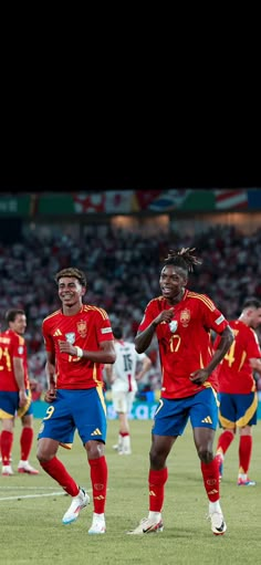 two soccer players in red and blue uniforms standing on the field with their arms around each other