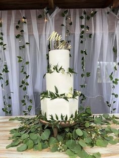 a white wedding cake with greenery on the side and mr and mrs topper