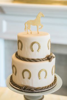 a three tiered cake with a horse decoration on the top, and gold accents