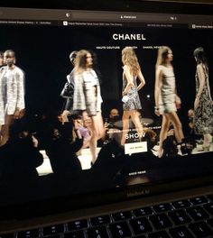 a laptop computer displaying a fashion show on it's display screen, with the image of models walking down the runway