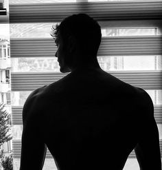 a man standing in front of a window with his back turned to the camera and looking out