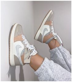 a woman's feet in white and grey sneakers with her leg up against the wall