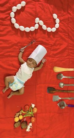 a baby laying on top of a red table covered in food and utensils