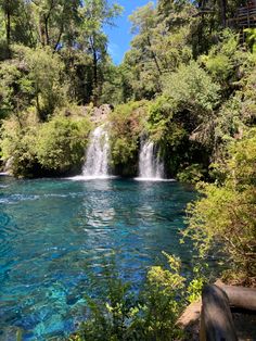 a waterfall in the middle of a river surrounded by trees and blue water with people on it