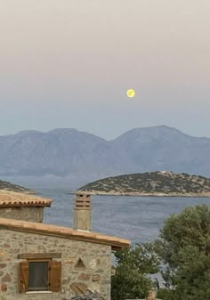 the moon is setting over an old stone building with mountains in the backgroud