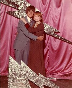 a man and woman hugging each other in front of a pink backdrop with silver foil