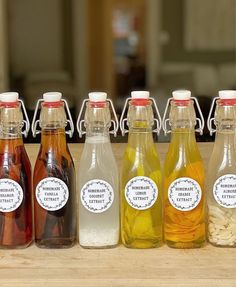 six different types of drinks are lined up on a counter top, with labels in each bottle