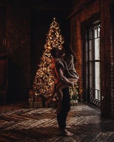 a woman is holding a man in front of a christmas tree with lights on it