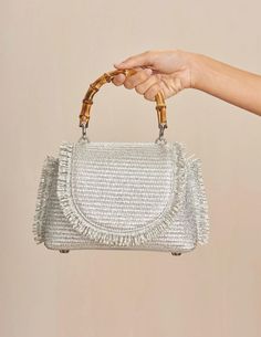 Cult Gaia Ozzy Mini Top Handle Bag in silver. Bamboo top handle. Woven raffia body. Fringe trim. Silver toned purse feet. Metallic coated raffia. W 3.94" X H 5.71" X L 8.66". HANDLE DROP: 2.91". 52% Cotton, 48% Polyamide. Trim: 100% Cow Leather. Lining: 90% Polyester, 10% Polyurethane. Imported. Silver Shoulder Bag With Top Handle And Detachable Handle, Silver Shoulder Bag With Top Carry Handle, Silver Top Handle Shoulder Bag With Detachable Strap, Silver Top Handle Shoulder Bag, Silver Handheld Shoulder Bag With Top Carry Handle, Silver Top Handle Shoulder Bag For Shopping, Silver Shoulder Bag For Summer Shopping, Silver Shoulder Bag For Summer, Chic Silver Shoulder Bag With Round Handle