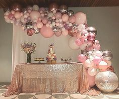 a table topped with lots of balloons next to a white and pink cake on top of a table