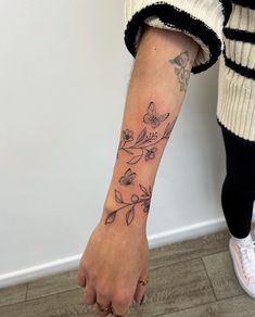 a woman's arm with flowers and butterflies tattooed on the left side of her arm