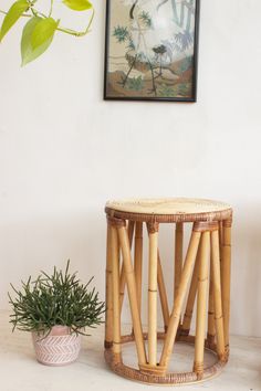 a small table next to a potted plant on a white floor with a painting above it