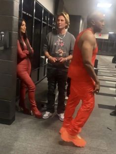 two men and a woman standing in front of lockers wearing red pants with orange shoes