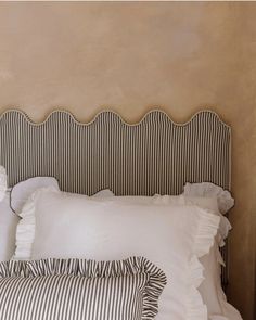 a bed with white pillows and black and white striped headboard against a tan wall